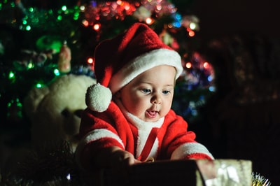 婴儿穿着圣诞老人的衣服靠近圣诞树

